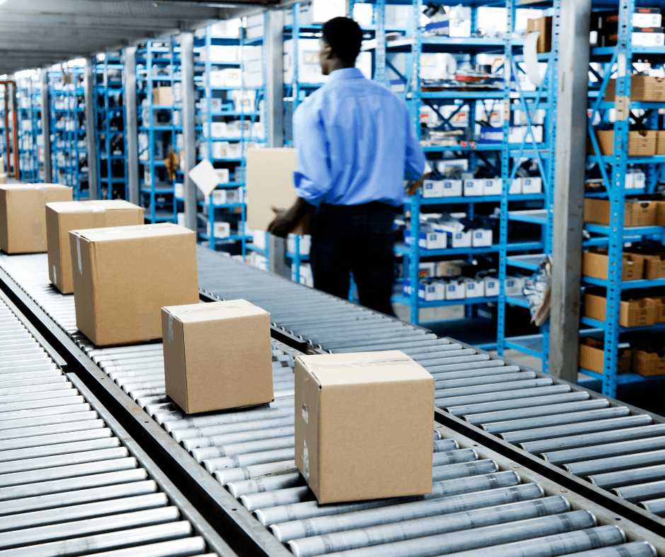 Convoyeur à bande dans un entrepôt avec des boîtes en carton et un employé en arrière-plan.