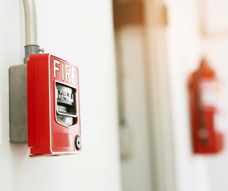 Ventouse électromagnétique de sécurité incendie fixée sur un mur, accompagnée d'un bouton d'alarme rouge et d'un extincteur en arrière-plan flou.
